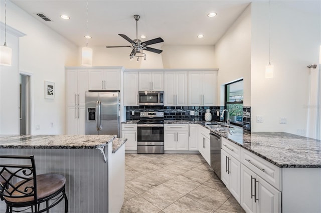 kitchen with kitchen peninsula, stainless steel appliances, decorative light fixtures, stone countertops, and white cabinets