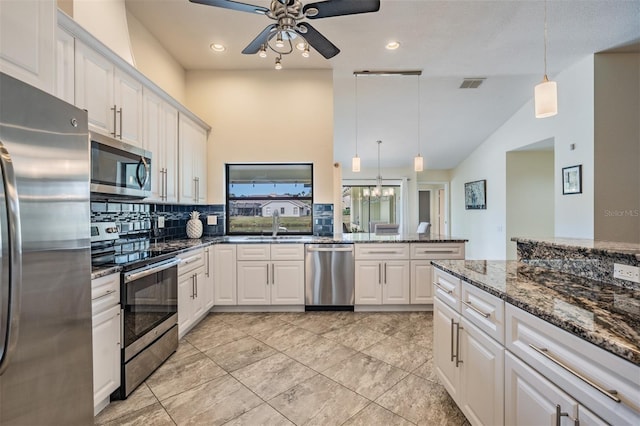 kitchen with lofted ceiling, white cabinets, dark stone countertops, appliances with stainless steel finishes, and decorative light fixtures