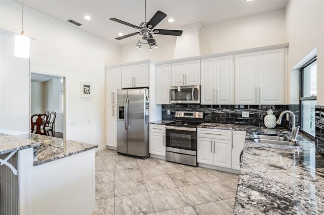 kitchen with sink, a towering ceiling, appliances with stainless steel finishes, stone countertops, and white cabinetry