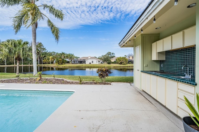 view of pool featuring a yard, a patio, a water view, and sink