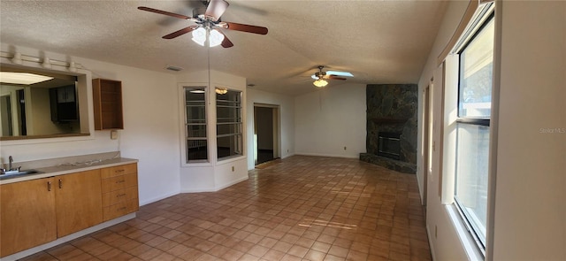 kitchen featuring sink, vaulted ceiling, a fireplace, and a textured ceiling