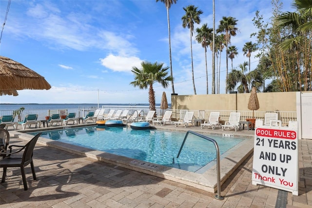 community pool with a patio area, a water view, and fence