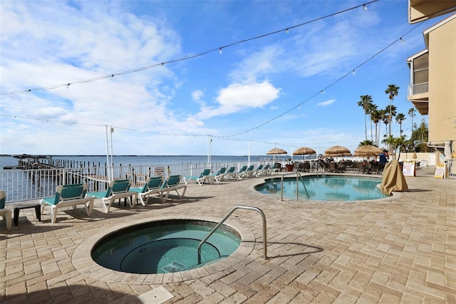 community pool featuring a community hot tub, a patio area, a water view, and fence