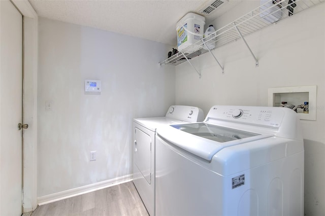 laundry area with light hardwood / wood-style floors, washing machine and dryer, and a textured ceiling