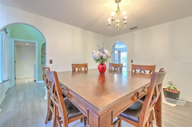 dining space with a textured ceiling, a chandelier, and light wood-type flooring