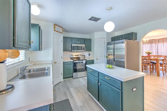 kitchen featuring sink, light hardwood / wood-style flooring, a textured ceiling, appliances with stainless steel finishes, and pendant lighting