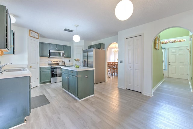 kitchen with sink, backsplash, stainless steel appliances, a kitchen island, and decorative light fixtures