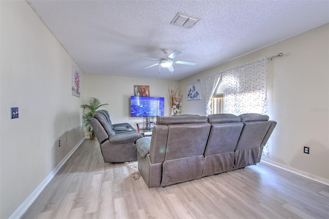 living room featuring ceiling fan, light hardwood / wood-style flooring, and a textured ceiling