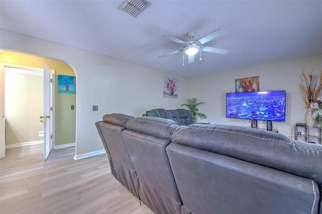 living room with a textured ceiling, ceiling fan, and light hardwood / wood-style flooring