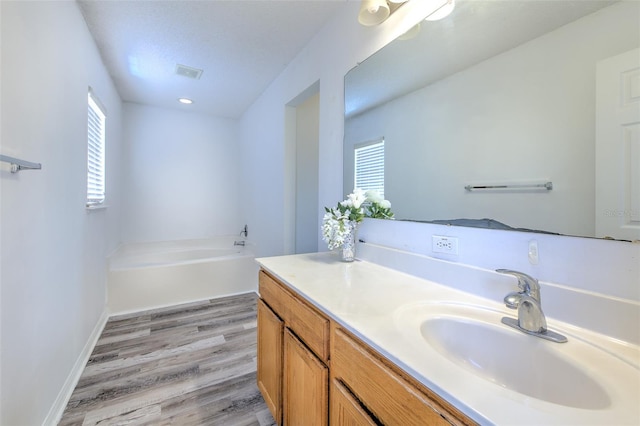 bathroom featuring wood-type flooring, a healthy amount of sunlight, a bath, and vanity