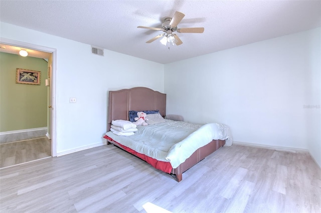 bedroom with ceiling fan, light hardwood / wood-style flooring, and a textured ceiling