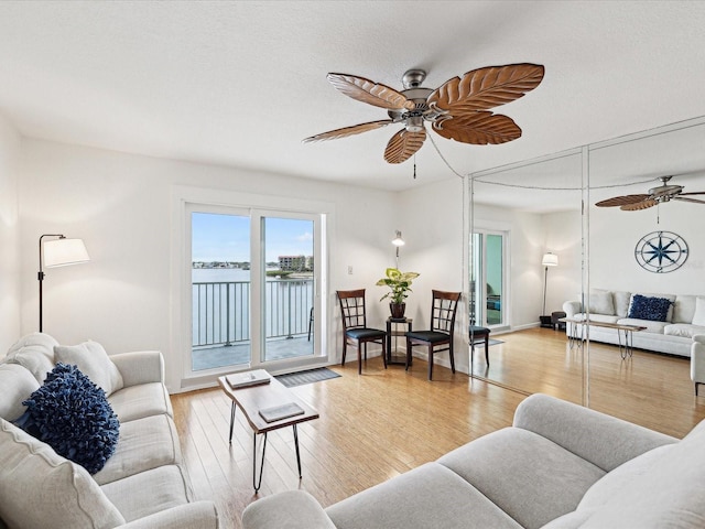 living room with a textured ceiling, light wood-type flooring, ceiling fan, and a water view