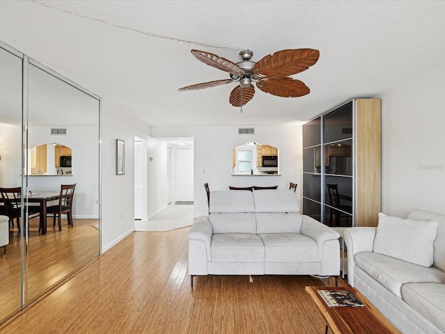 living room with light wood-type flooring, ceiling fan, and a textured ceiling