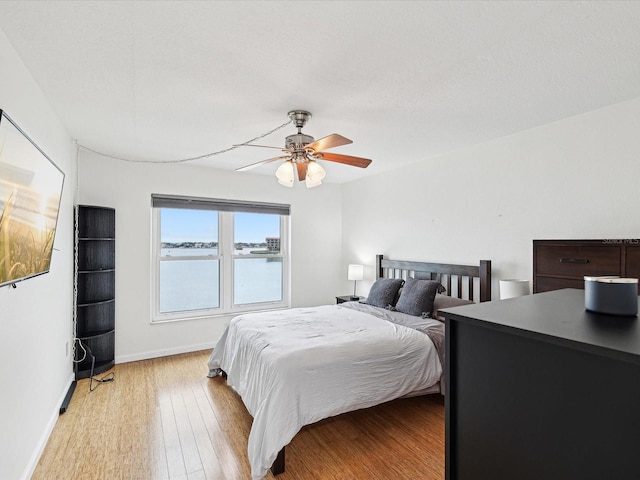 bedroom with ceiling fan, light wood-type flooring, and a water view