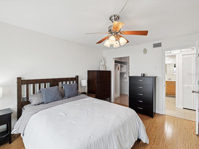 bedroom featuring ensuite bathroom, a closet, light wood-type flooring, a walk in closet, and ceiling fan