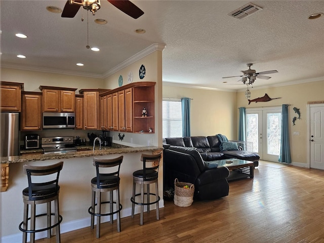 kitchen with hardwood / wood-style floors, dark stone counters, french doors, appliances with stainless steel finishes, and a breakfast bar area