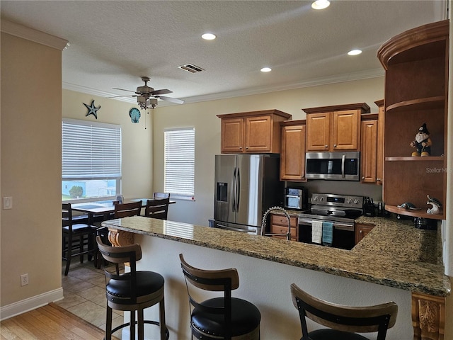 kitchen with appliances with stainless steel finishes, a textured ceiling, ornamental molding, and dark stone countertops