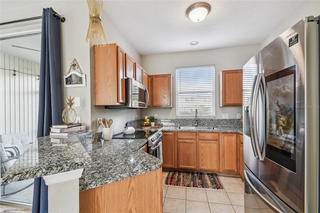 kitchen with sink, kitchen peninsula, dark stone countertops, light tile patterned floors, and appliances with stainless steel finishes