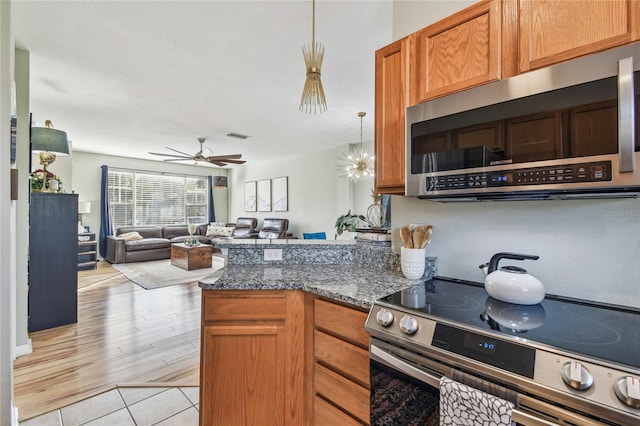 kitchen with ceiling fan, kitchen peninsula, pendant lighting, dark stone counters, and appliances with stainless steel finishes