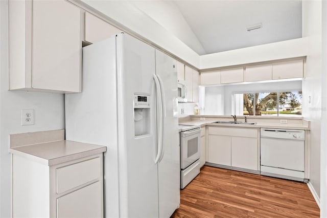 kitchen with white appliances, vaulted ceiling, sink, white cabinets, and light hardwood / wood-style floors