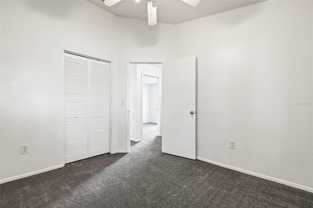 unfurnished bedroom with dark colored carpet, a towering ceiling, a closet, and ceiling fan