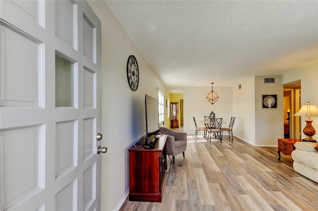 interior space featuring light wood-type flooring, a textured ceiling, and an inviting chandelier