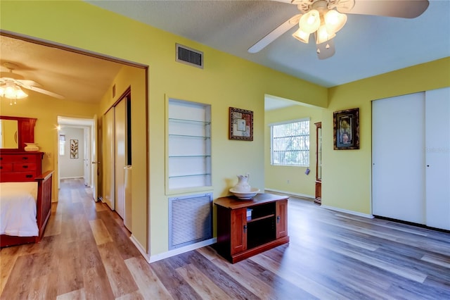 hallway with built in shelves, light wood-type flooring, and a textured ceiling