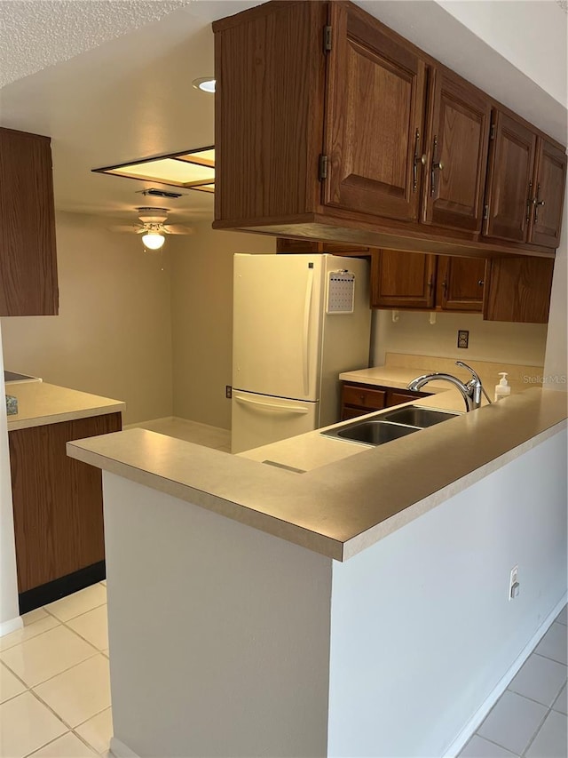 kitchen with white fridge, kitchen peninsula, sink, and light tile patterned floors