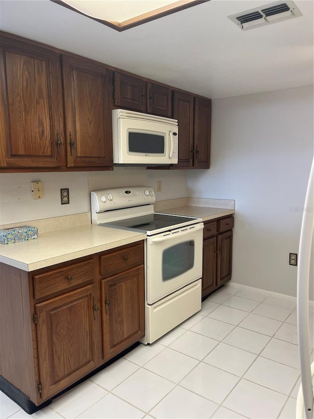 kitchen with light tile patterned floors, white appliances, and dark brown cabinetry