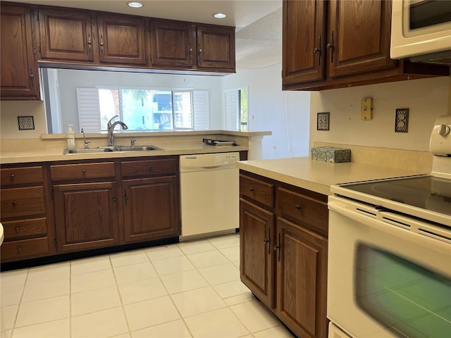 kitchen featuring dark brown cabinets, light tile patterned flooring, white appliances, and sink