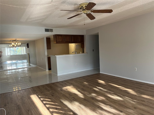 unfurnished living room featuring ceiling fan with notable chandelier, light tile patterned flooring, and a textured ceiling