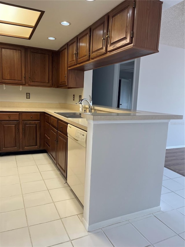 kitchen featuring white dishwasher, sink, light tile patterned floors, dark brown cabinets, and kitchen peninsula