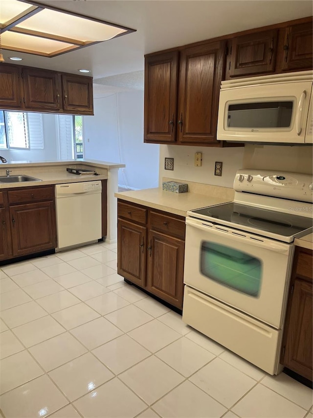 kitchen featuring light tile patterned flooring, white appliances, dark brown cabinetry, and sink