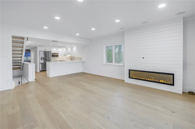 unfurnished living room featuring a large fireplace, sink, and light hardwood / wood-style floors