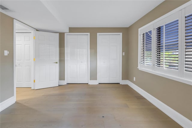 unfurnished bedroom with light wood-type flooring and two closets