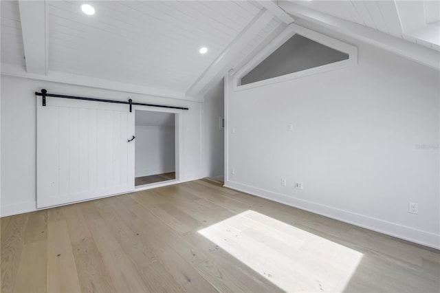 unfurnished bedroom with lofted ceiling with beams, a closet, a barn door, and light hardwood / wood-style flooring