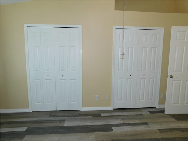 unfurnished bedroom featuring vaulted ceiling, dark hardwood / wood-style flooring, and two closets