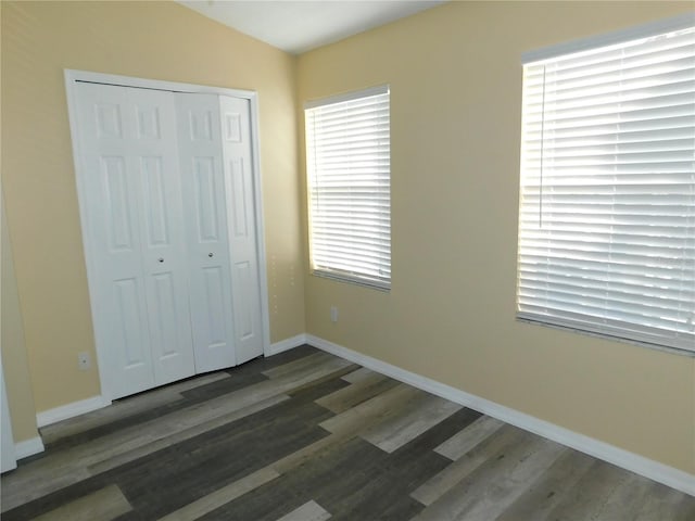 unfurnished bedroom featuring a closet, vaulted ceiling, baseboards, and wood finished floors