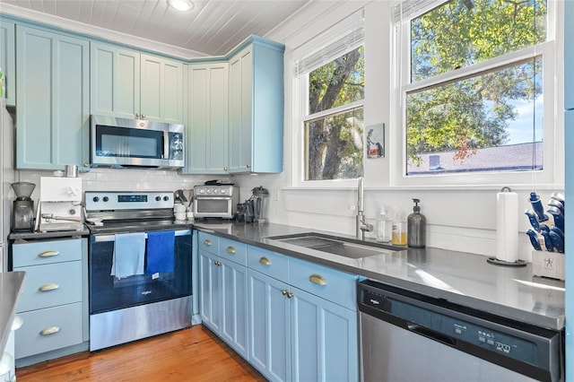 kitchen with blue cabinets, crown molding, sink, light wood-type flooring, and stainless steel appliances