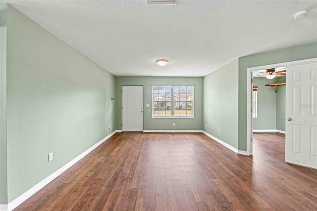 empty room with a textured ceiling, dark wood-type flooring, a ceiling fan, and baseboards