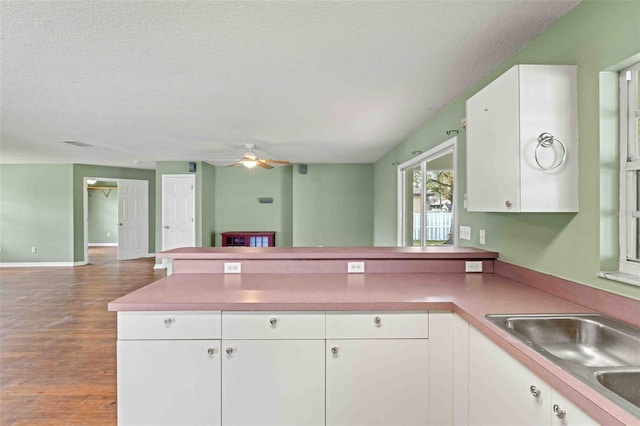 kitchen with open floor plan, a peninsula, a textured ceiling, white cabinetry, and a sink