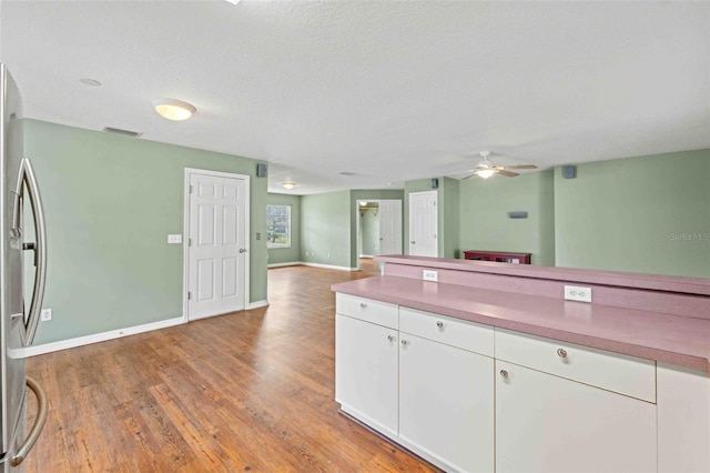 kitchen with wood finished floors, visible vents, white cabinets, open floor plan, and freestanding refrigerator