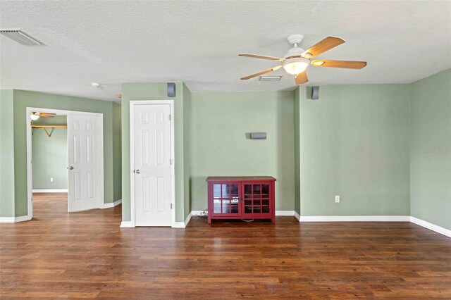 empty room with dark wood-style flooring, visible vents, and baseboards