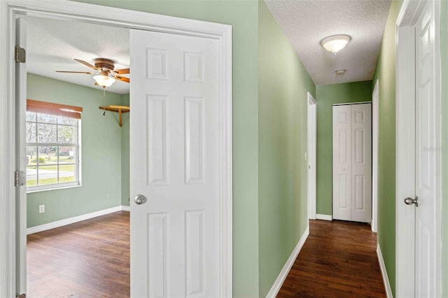 hallway featuring dark wood-type flooring, a textured ceiling, and baseboards