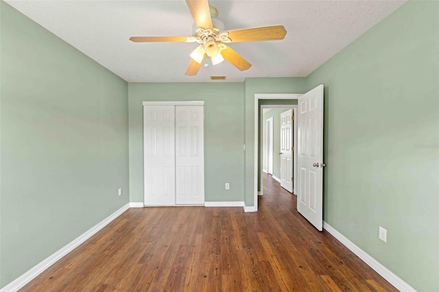 unfurnished bedroom with a closet, dark wood-style flooring, ceiling fan, and baseboards