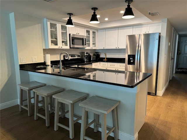 kitchen featuring a raised ceiling, hanging light fixtures, appliances with stainless steel finishes, white cabinetry, and kitchen peninsula