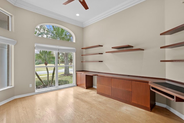 unfurnished office featuring light wood-type flooring, ceiling fan, ornamental molding, and built in desk