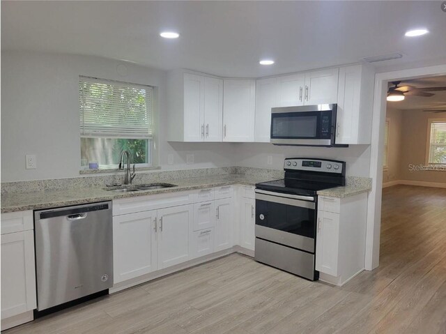 kitchen with white cabinets, sink, light stone countertops, light hardwood / wood-style floors, and stainless steel appliances