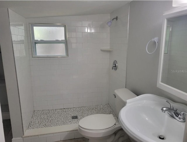 bathroom featuring a tile shower, sink, and toilet