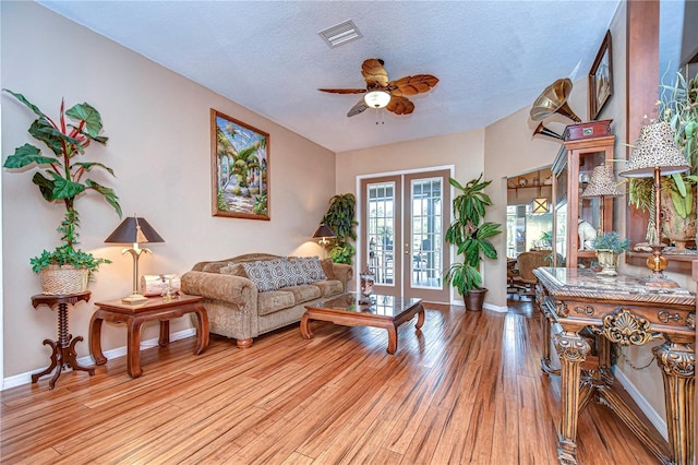 living room featuring a textured ceiling, french doors, ceiling fan, and light wood-type flooring